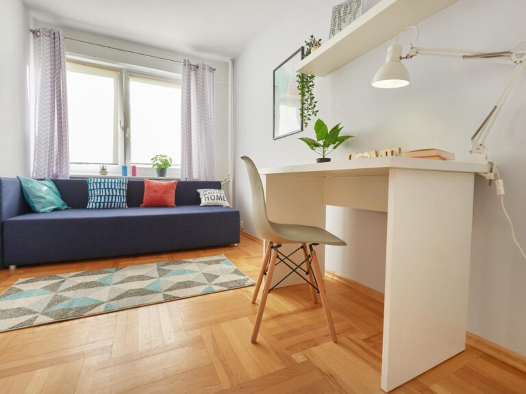 Sypialnia z granatową kanapą i miejscem do pracy. Niezłe Lokum przygotowało ten pokój do odpoczynku i nauki.