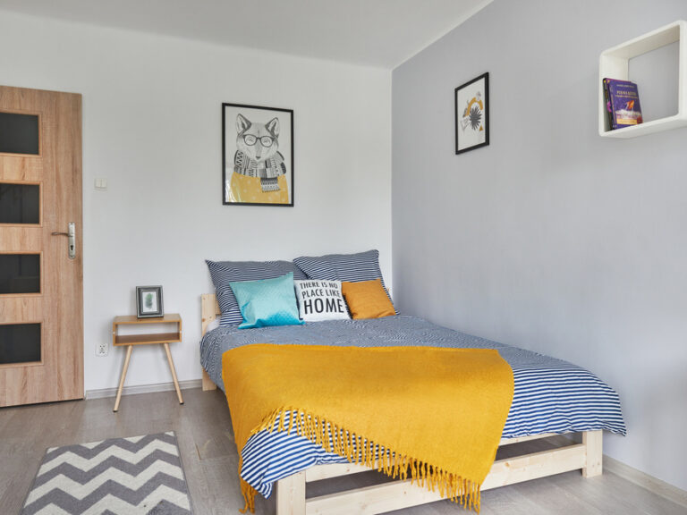 Wygodne łóżko w szarej sypialni z niebieskimi zasłonami, mieszkanie przy ul. Ofiar Katynia 10 w Rzeszowie. Szerokie łóżko o szerokości 160 cm, idealne dla pary. Niezłe Lokum zadbało o komfort lokatorów.